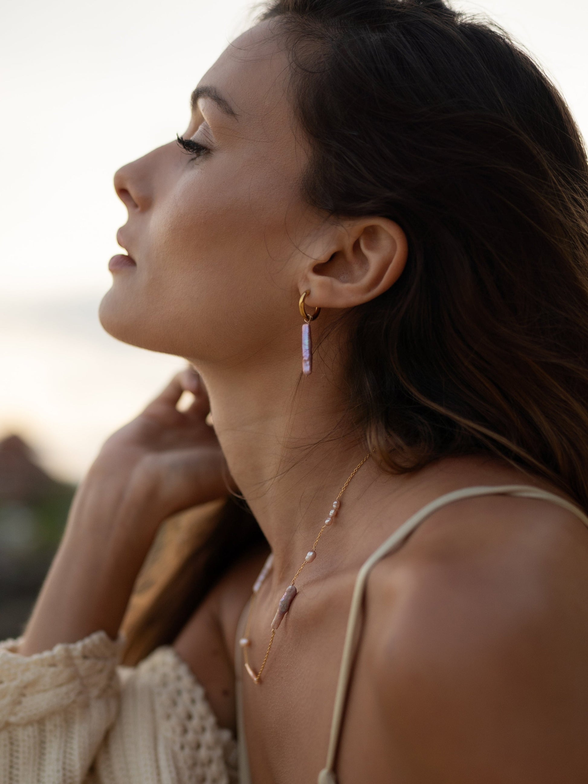 Woman wearing gold earrings and a necklace with a blurred background