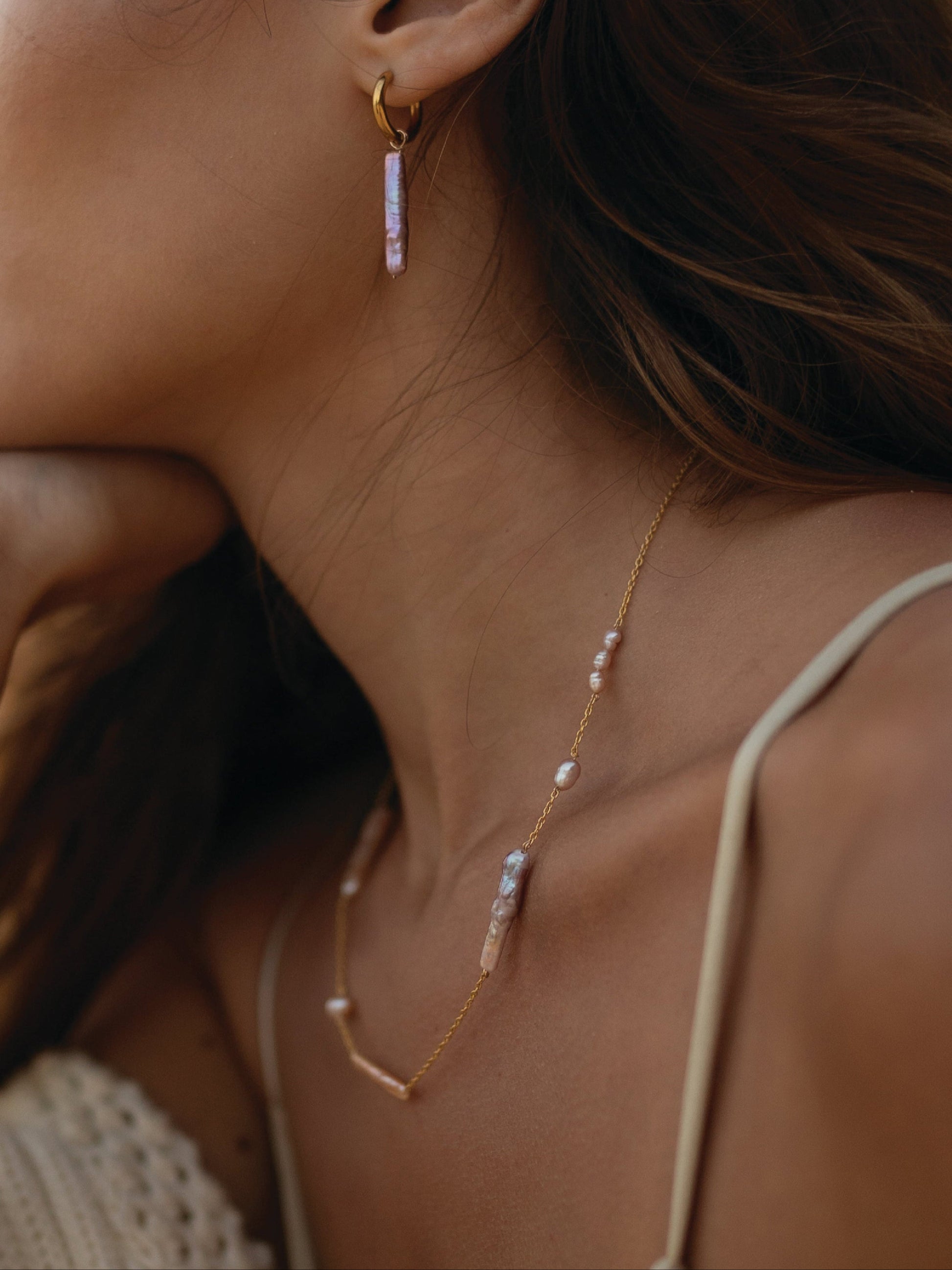 Close-up of a woman wearing gold hoop earrings and a delicate gold necklace with pearls.