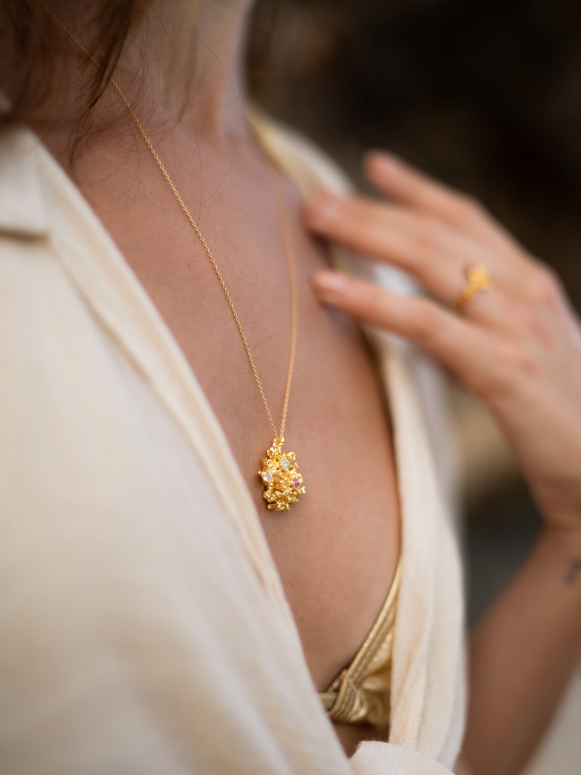 Gold necklace and ring on a person wearing a white blouse.