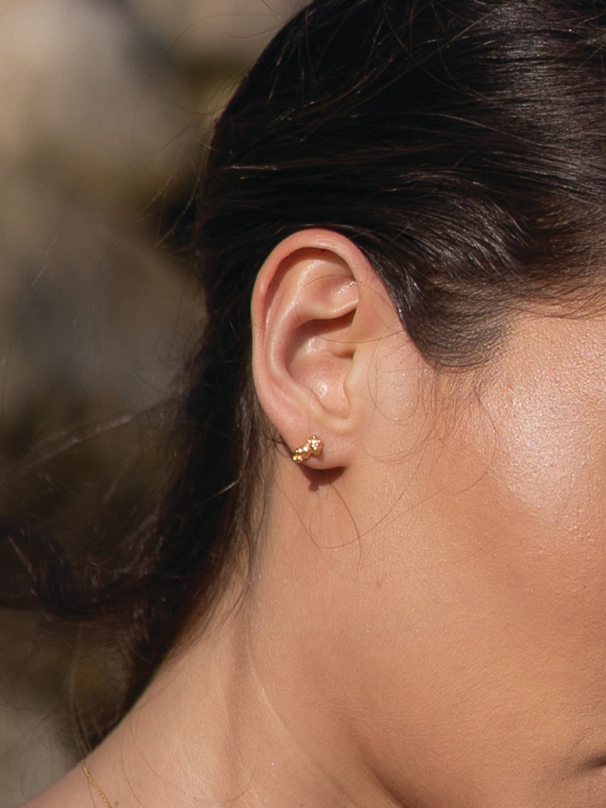 Close-up of a person wearing a gold earring with a blurred natural background