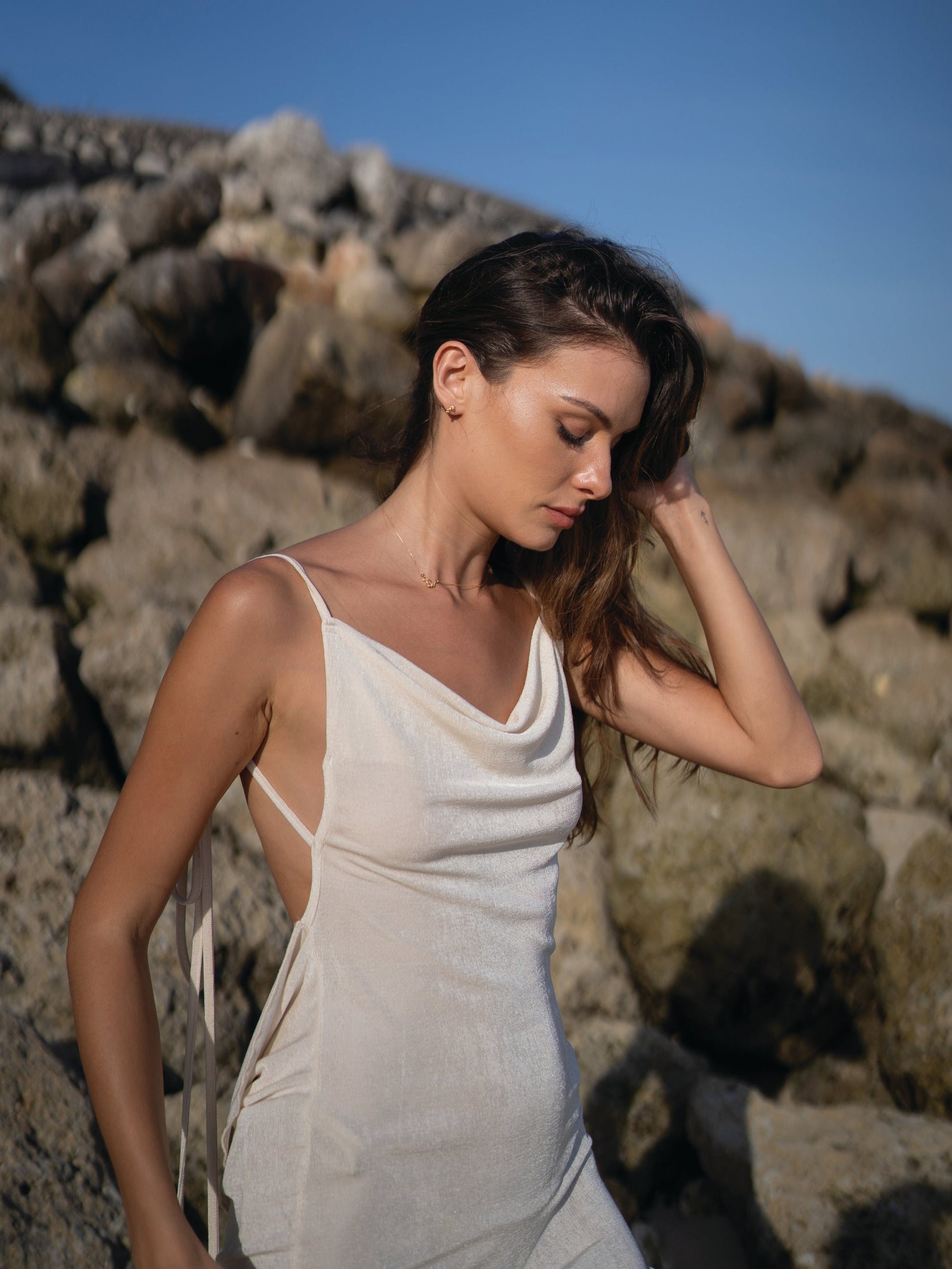 Woman in a light dress standing against a rocky background