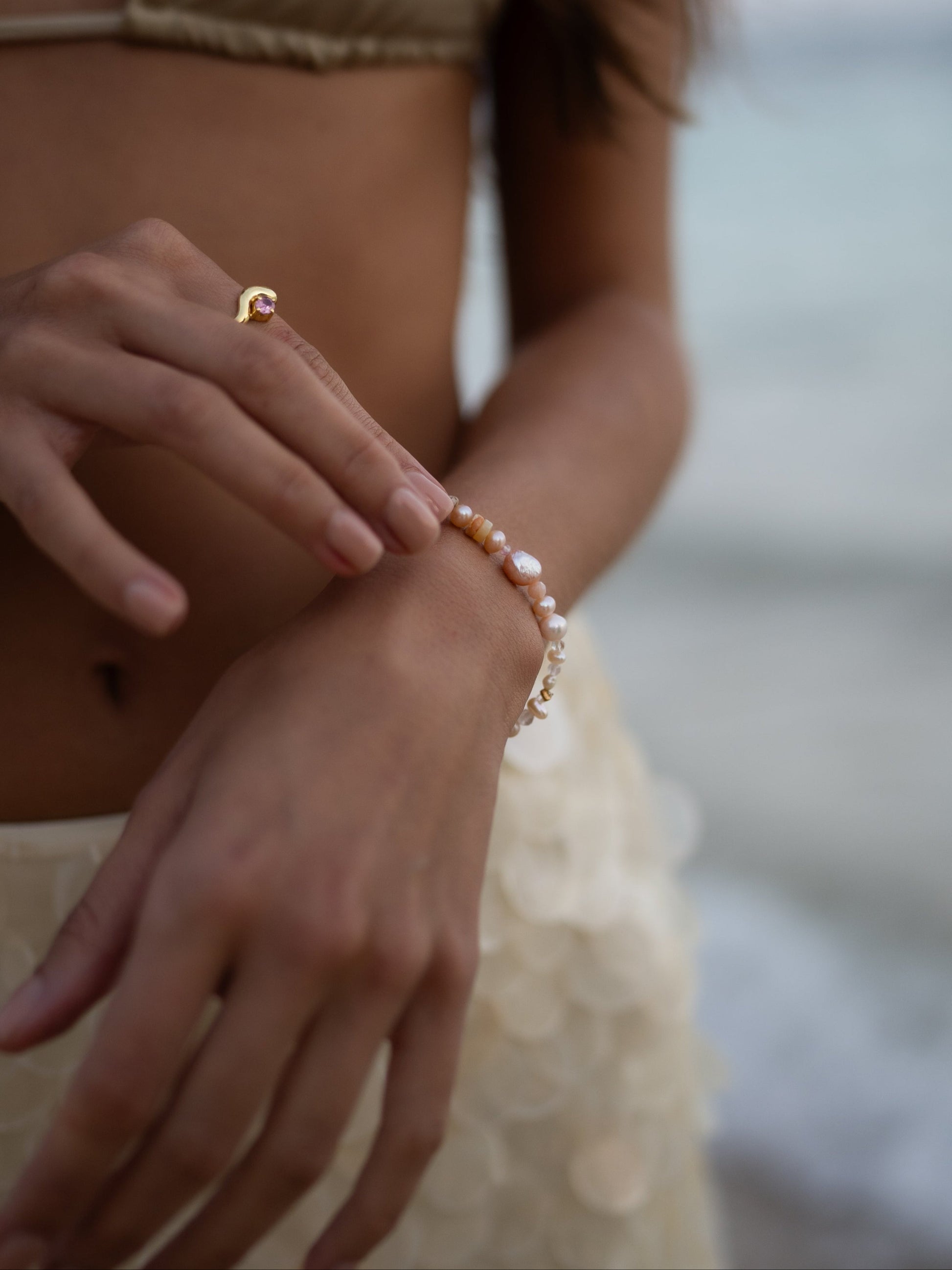 Close-up of a person wearing a pearl bracelet with a blurred beach background