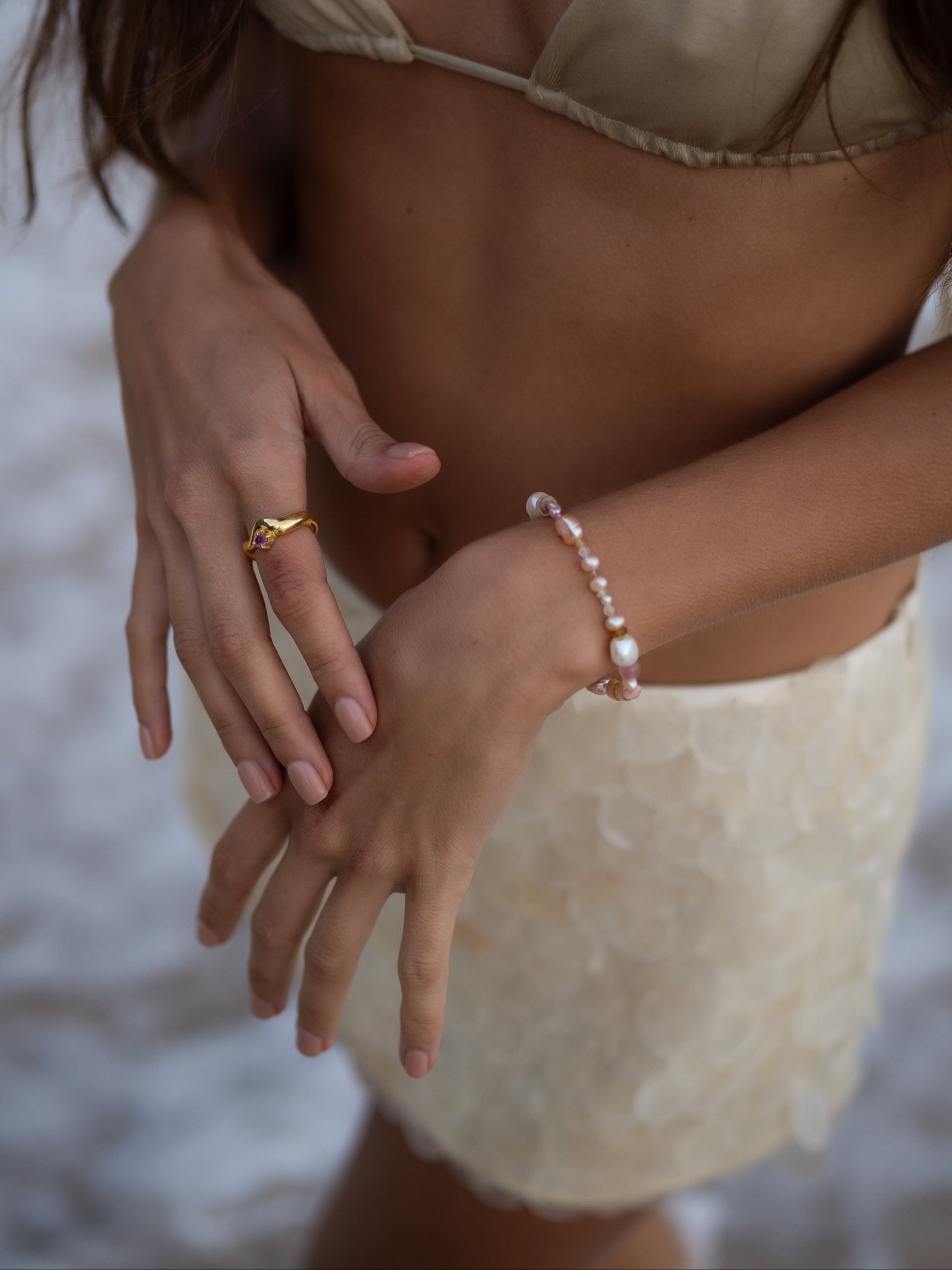 Close-up of a person wearing a gold ring and pearl bracelet on a blurred background