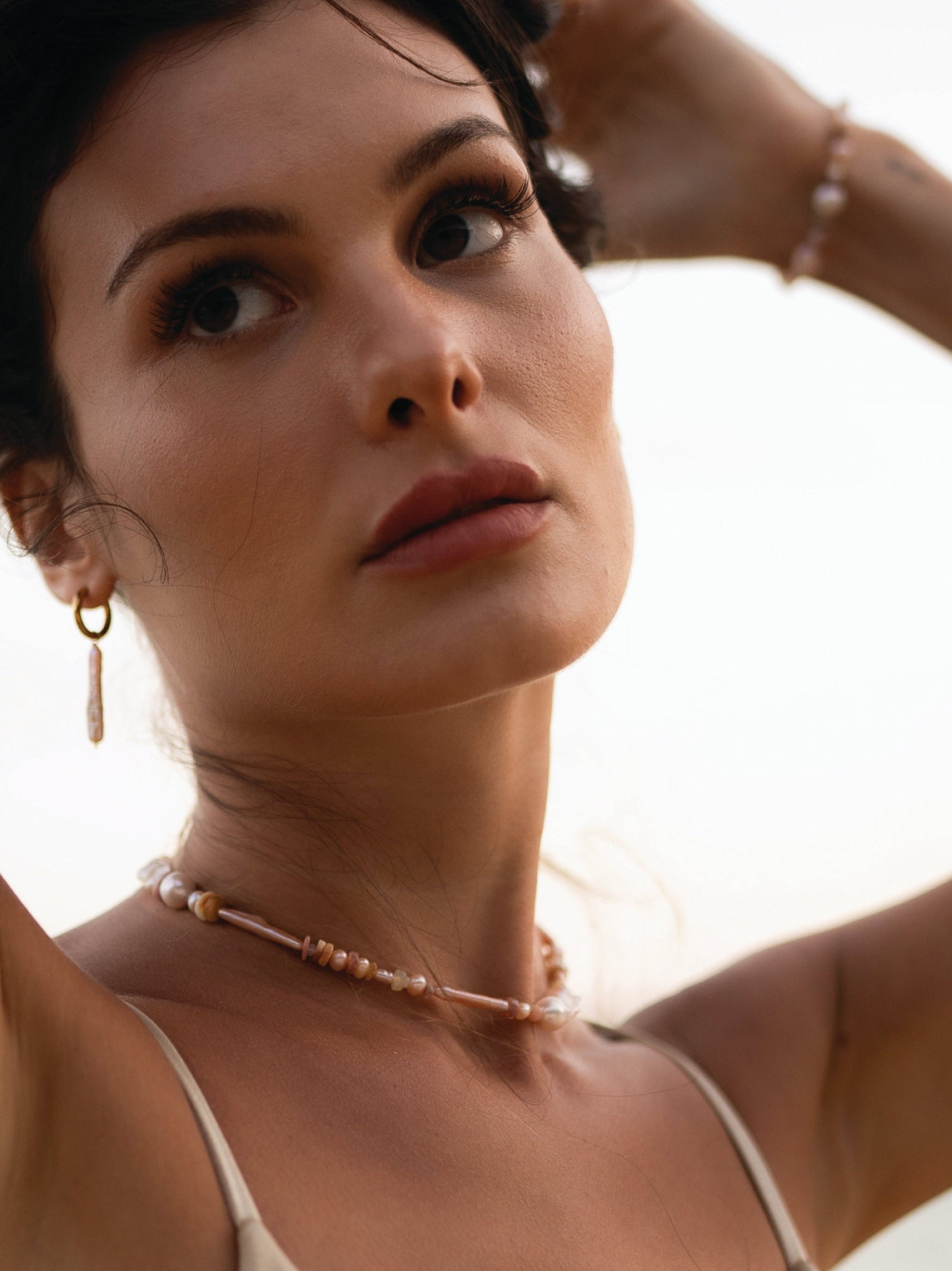 Close-up of a woman with a necklace and earrings against a blurred background