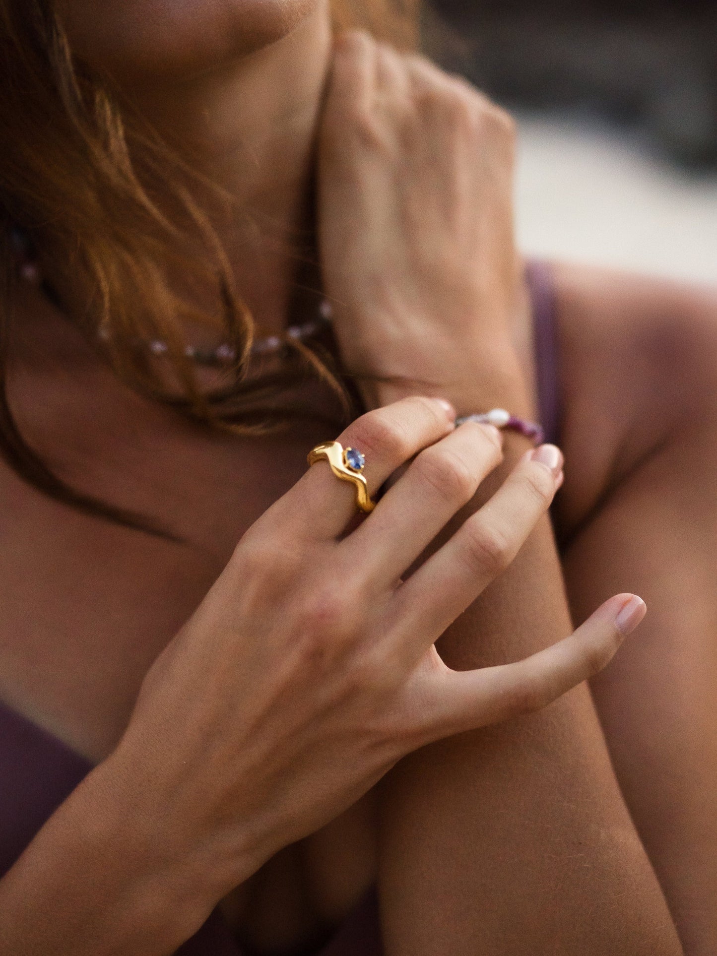 Close-up of a person's hand wearing a gold ring with a diamond on a blurred background