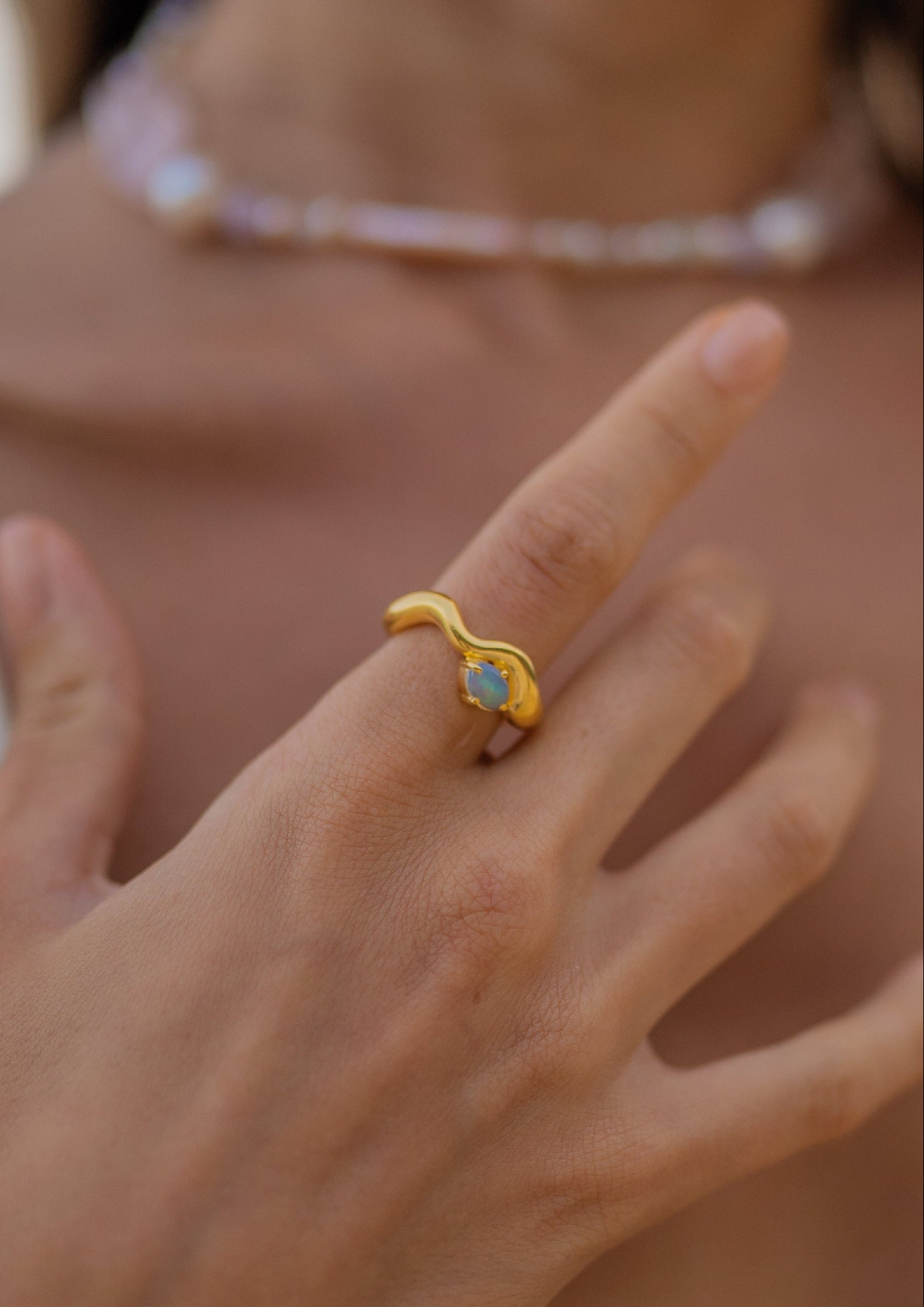 Close-up of a hand wearing a gold ring with a green gemstone, blurred background