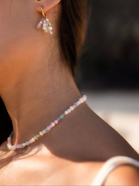 Close-up of a person wearing colorful beaded earrings and a necklace against a blurred background