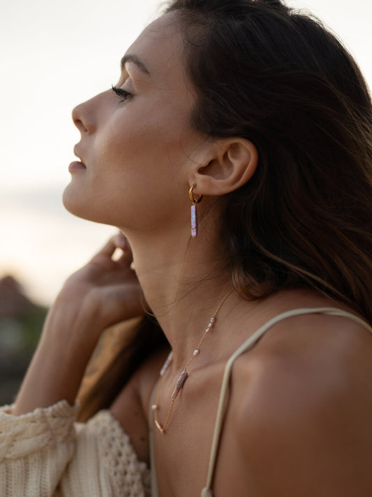 Woman wearing gold earrings and a necklace with a blurred background