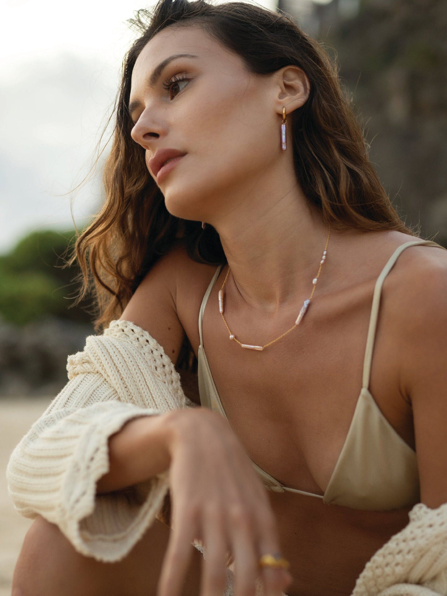 Woman in a green bikini top sitting on a beach with a blurred natural background