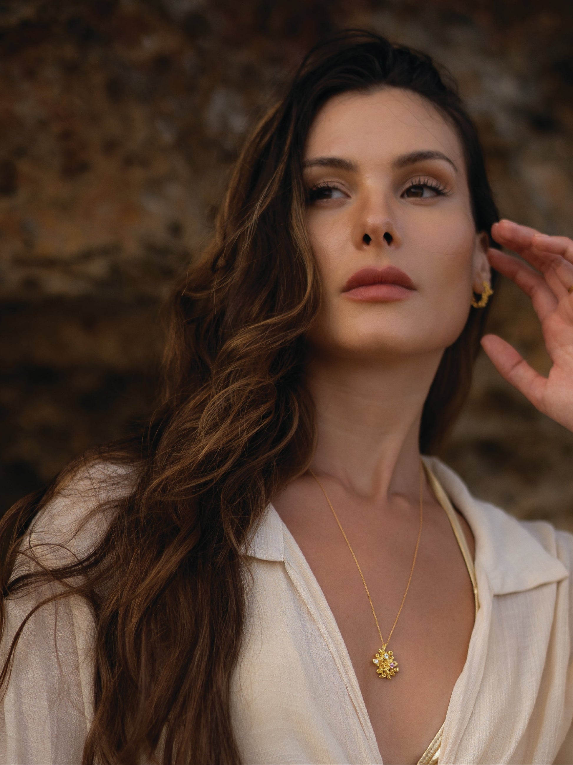 Woman wearing a gold necklace with a yellow pendant against a blurred natural background