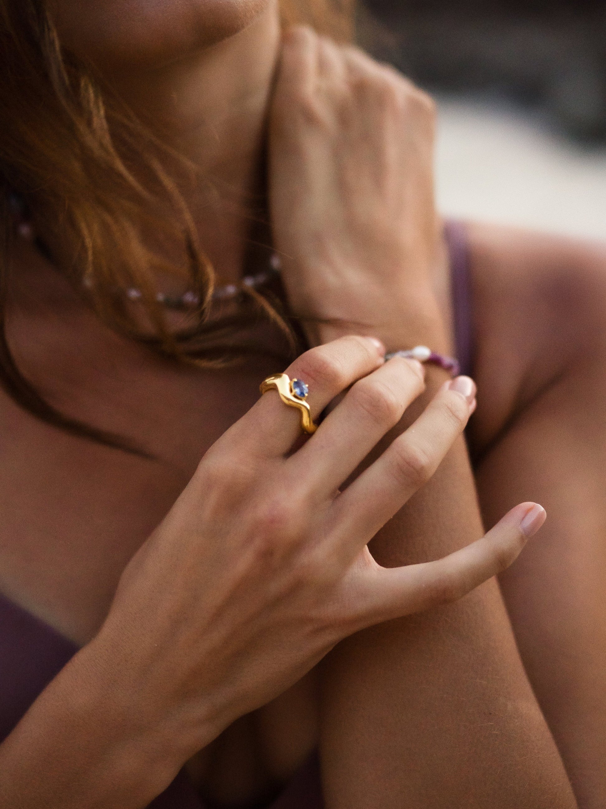 Close-up of a person's hand wearing a gold ring with a diamond on a blurred background